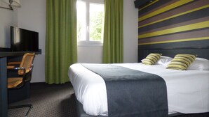 A hotel room with a bed, a desk with a chair, a television, and green curtains. - Brit Hotel Confort Villefranche de Rouergue (Villefranche-de-Rouergue)