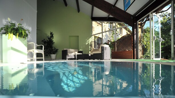 An indoor swimming pool with a clear view of the surrounding area, including a seating area with chairs and a table, and a green wall. - Brit Hotel Confort Villefranche de Rouergue (Villefranche-de-Rouergue)