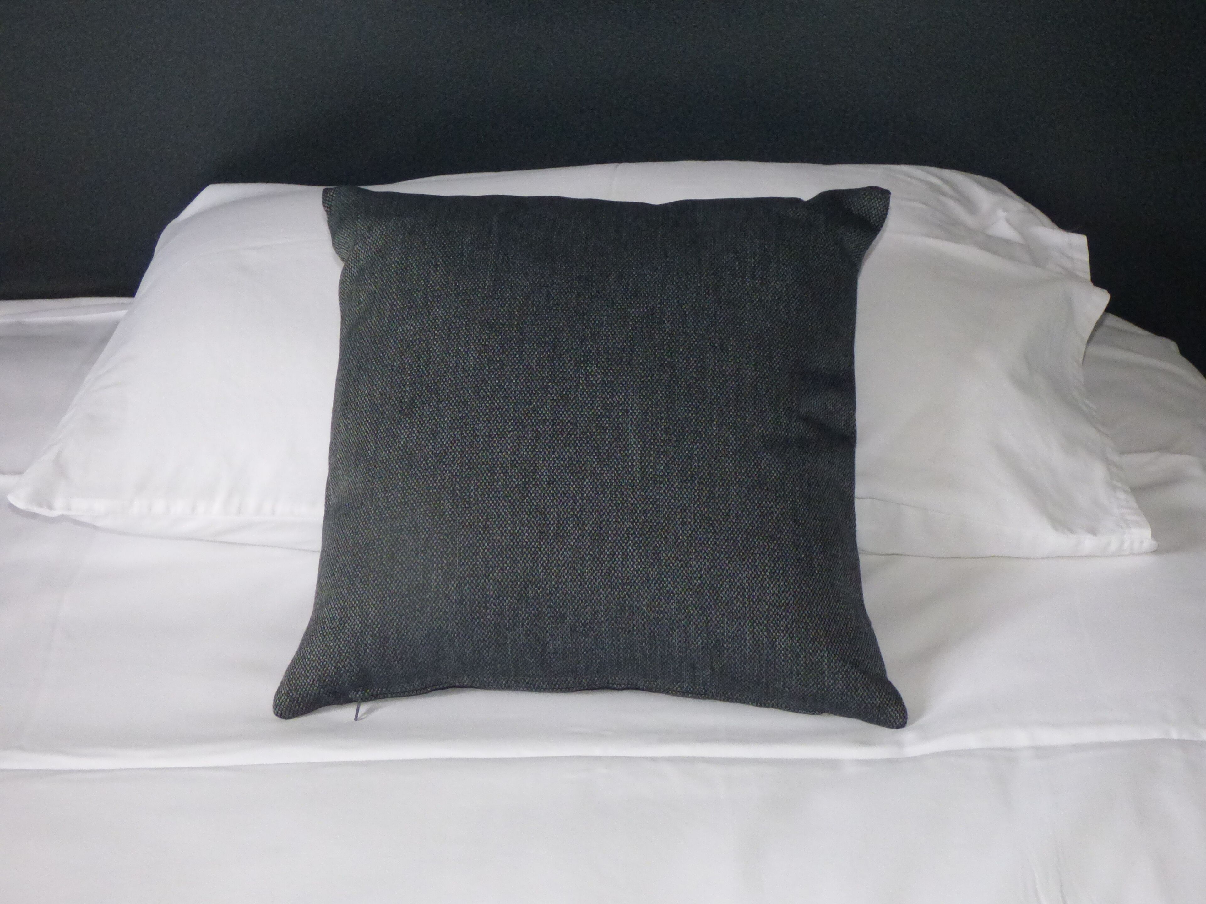 A bed with white linens and a single dark gray pillow.