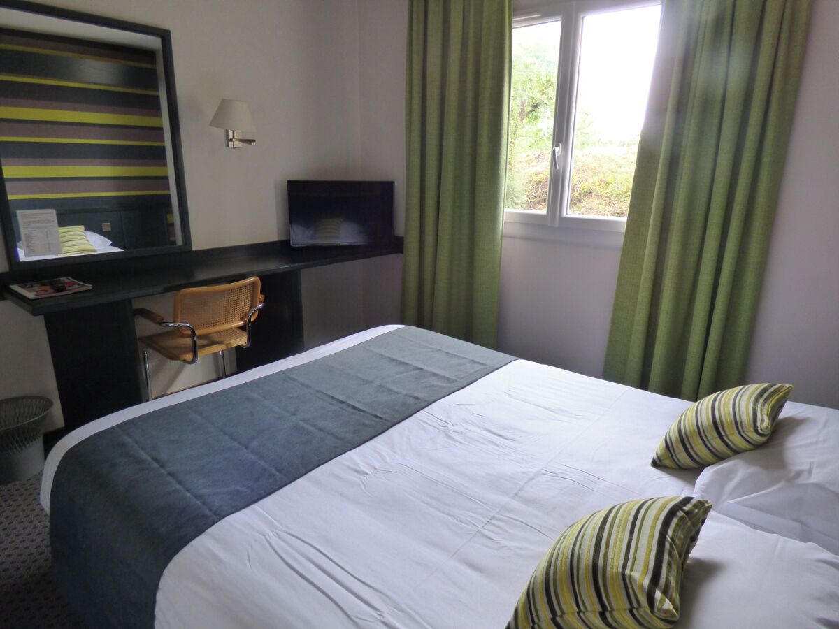 A hotel room with a bed, a desk, a chair, and a window with curtains.