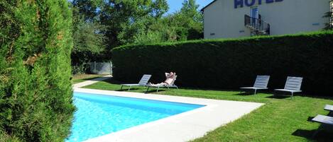 Un hotel con piscina, sillones de descanso y seto.