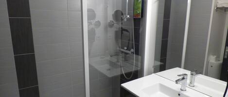 A modern bathroom with a glass-enclosed shower, a white sink with a mirror, and dark tiles on the walls.