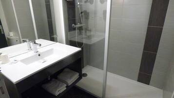 Un baño moderno con lavamanos blanco, ducha con cerramiento de vidrio y espejo sobre el lavamanos.