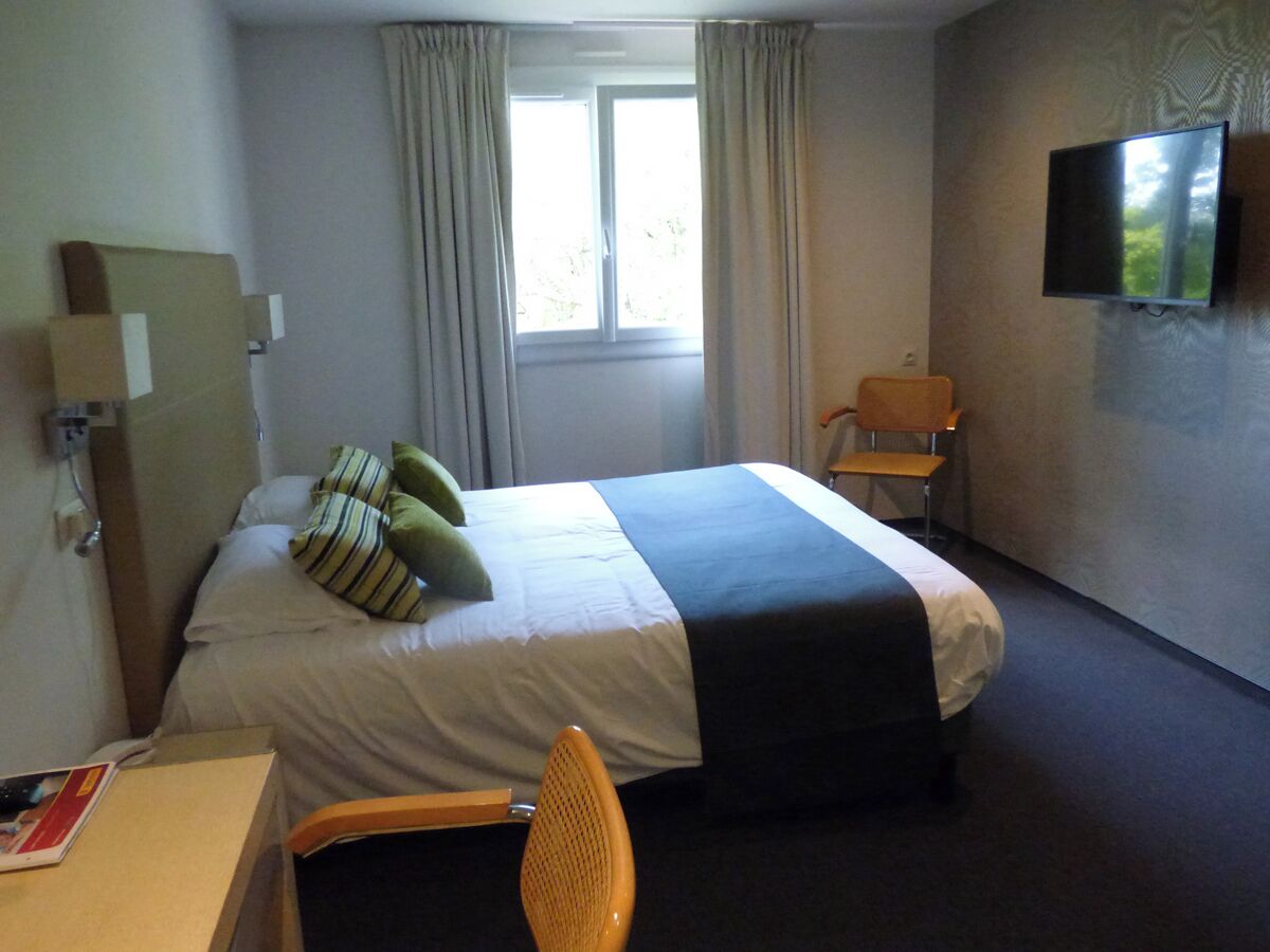 A hotel room with a bed, a desk, a chair, a TV, and a window with curtains.