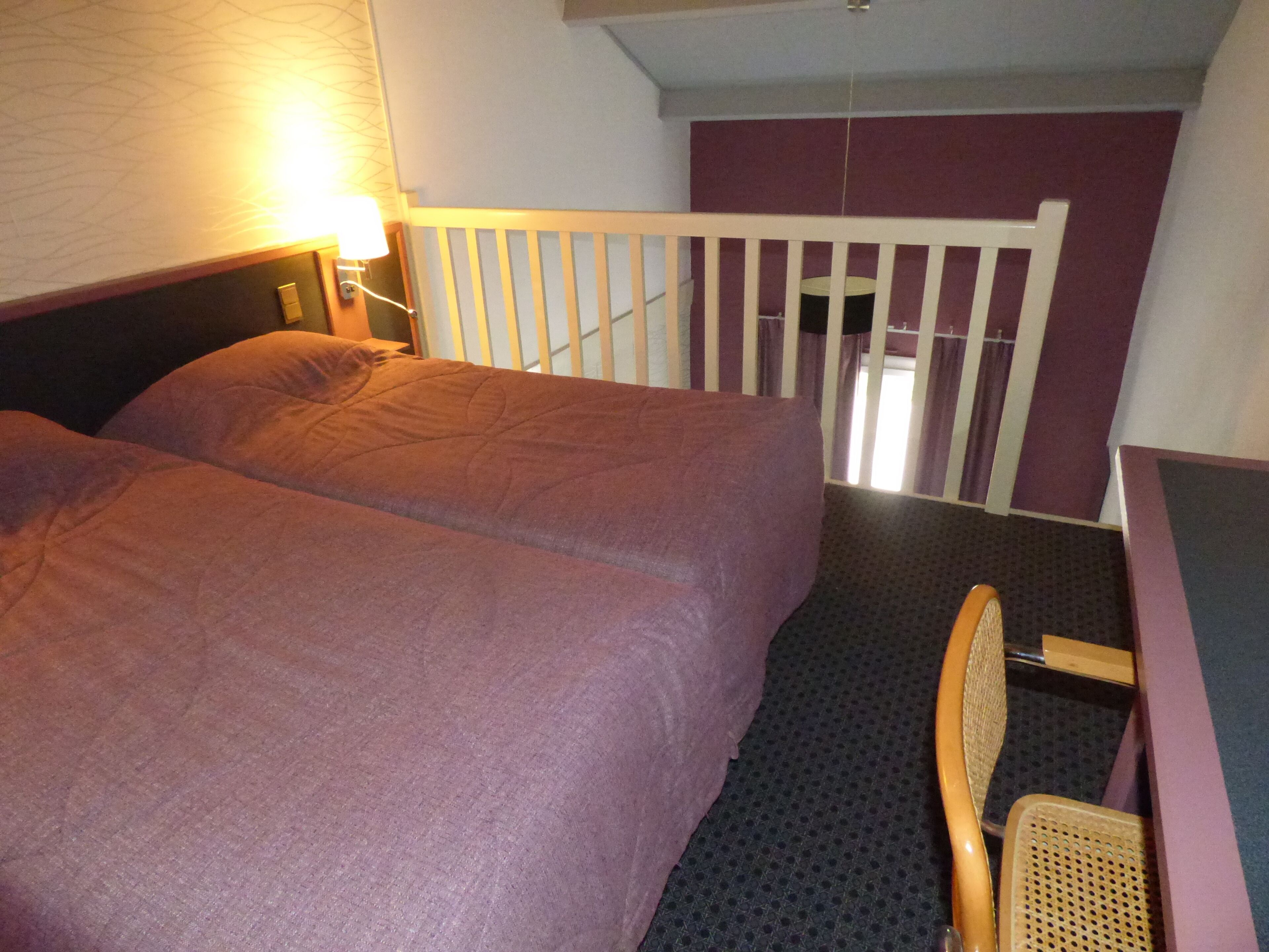 A small, compact room with a single bed, a chair, and a desk.