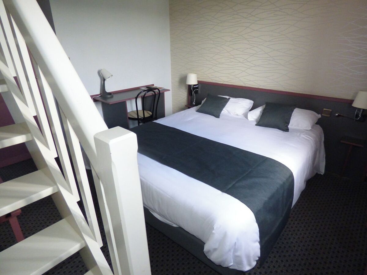 A hotel room with a bed, two bedside tables, a chair, and a staircase.