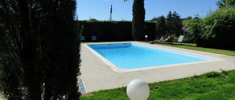 A rectangular swimming pool with a light-colored deck, surrounded by grass and trees.