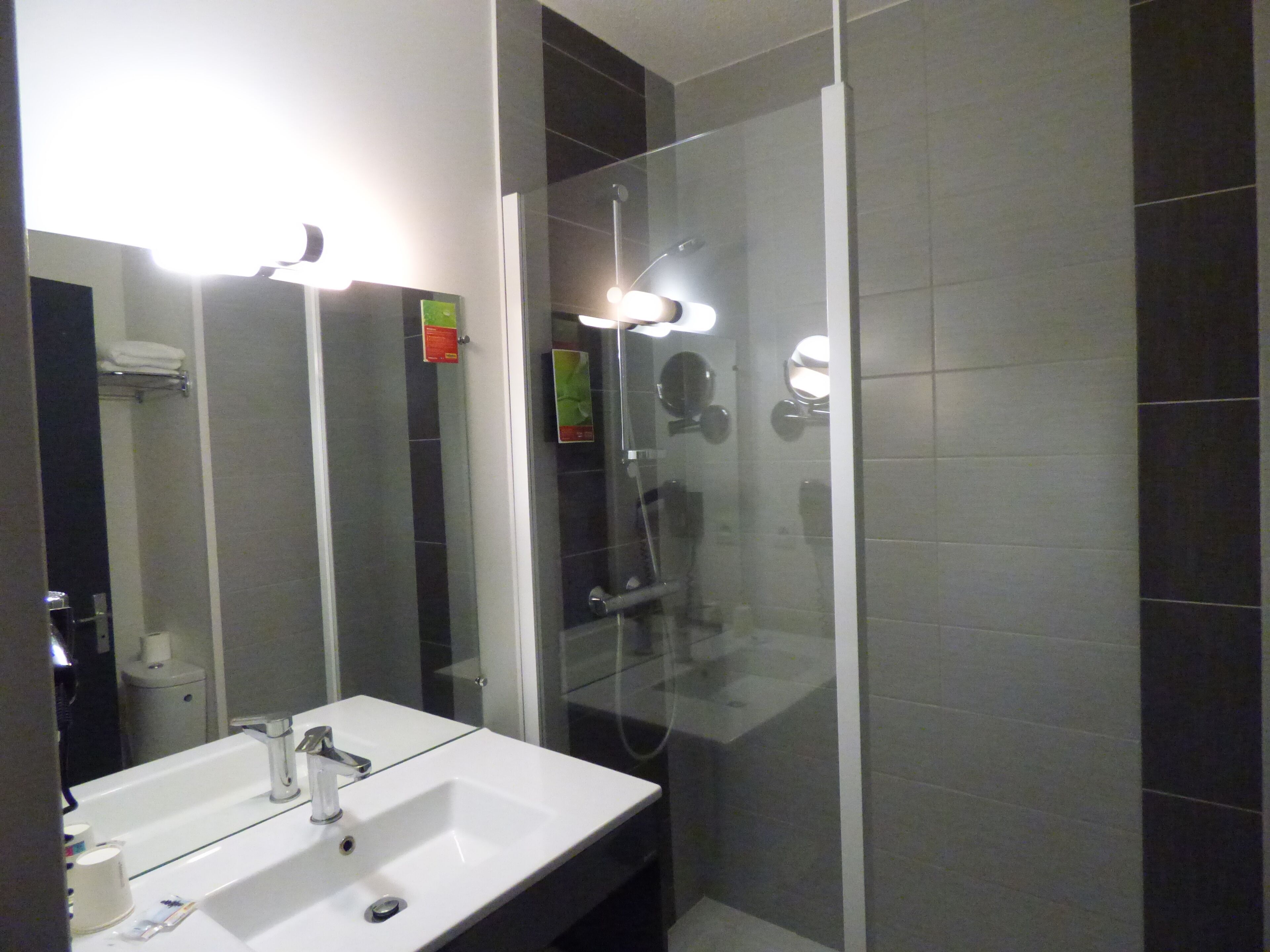 A modern bathroom with a white sink, glass shower enclosure, and dark tiled walls.