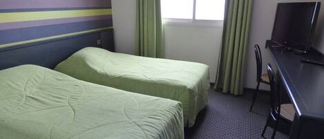 Una habitación de hotel con dos camas, un escritorio con televisor y una ventana con cortinas.