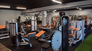 A gym with various exercise machines, benches, and a clock on the wall. - Brit Hotel Confort Villefranche de Rouergue (Villefranche-de-Rouergue)