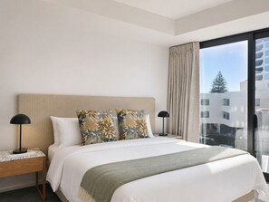 Habitación de hotel con una cama grande, dos mesitas de noche, una lámpara, una ventana con cortinas y vistas a edificios.