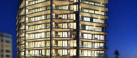 Un hotel de varios pisos con un diseño moderno, que cuenta con balcones y una zona de piscina.