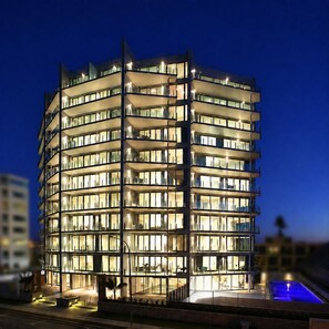 Un hotel de varios pisos con un diseño moderno, que cuenta con balcones y una zona de piscina.