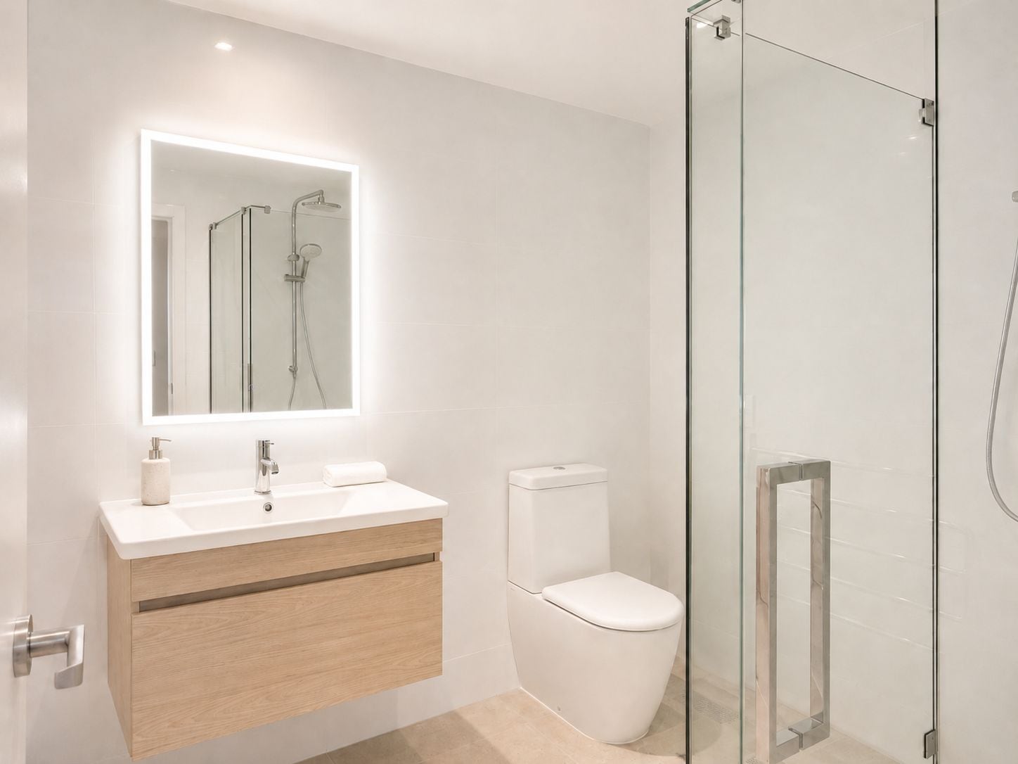 Un baño moderno con cabina de ducha de vidrio, inodoro blanco y tocador con espejo sobre el lavabo.