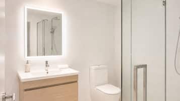 Un baño moderno con cabina de ducha de vidrio, inodoro blanco y tocador con espejo sobre el lavabo.