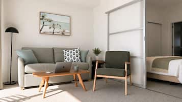 A modern living room with a sofa, a coffee table, a laptop, a chair, and a bed with a sliding door.
