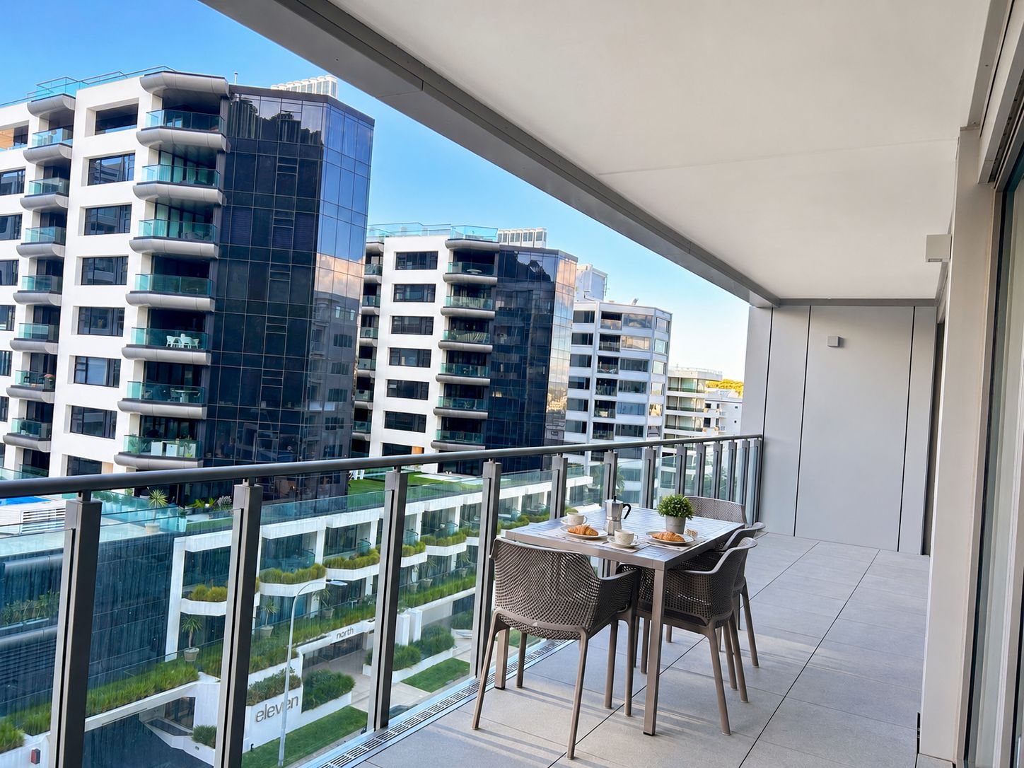 A balcony with a table and chairs, overlooking a modern residential building complex.