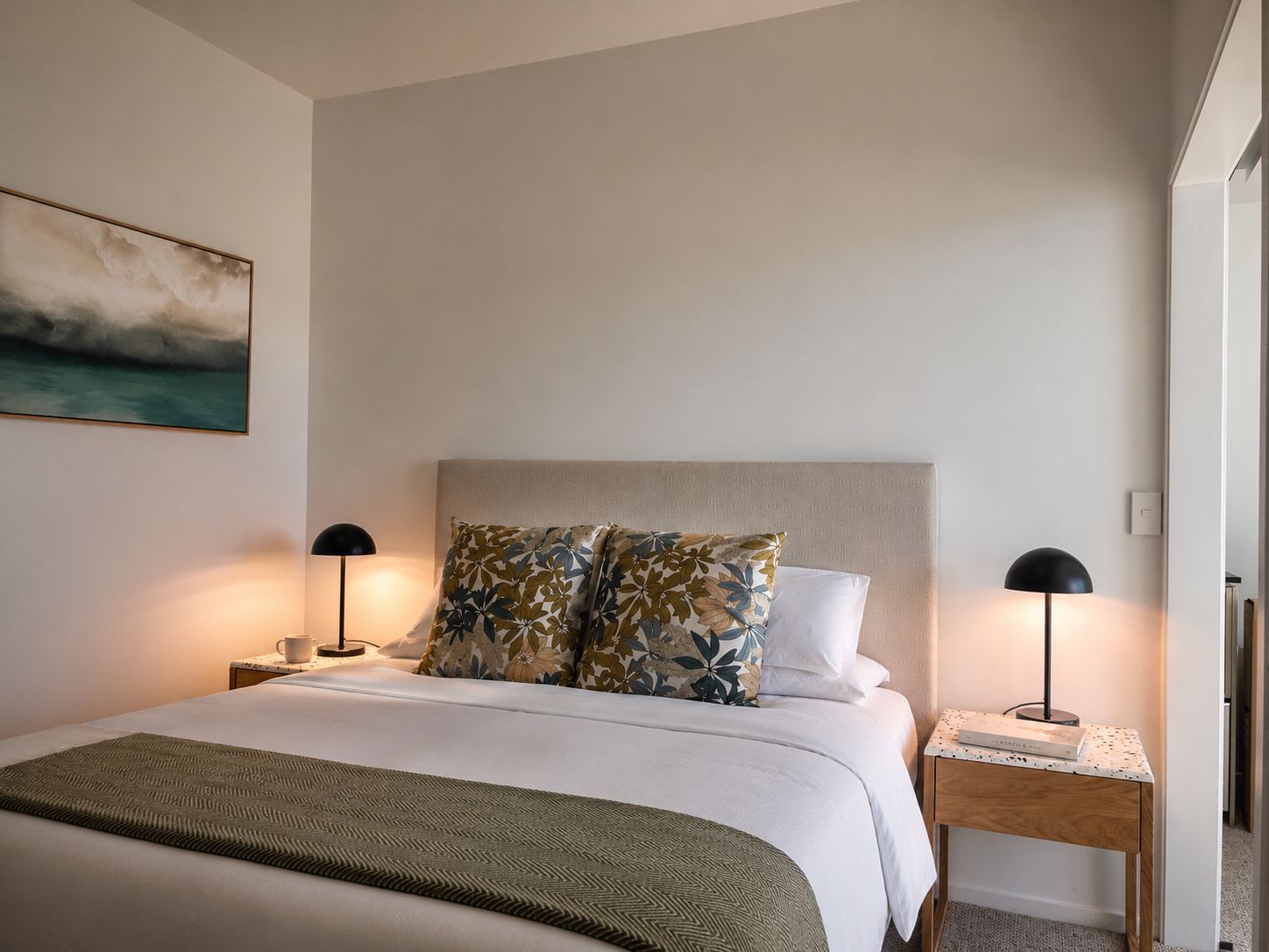 A neatly made bed with a green throw, two pillows with a floral pattern, and two bedside lamps.
