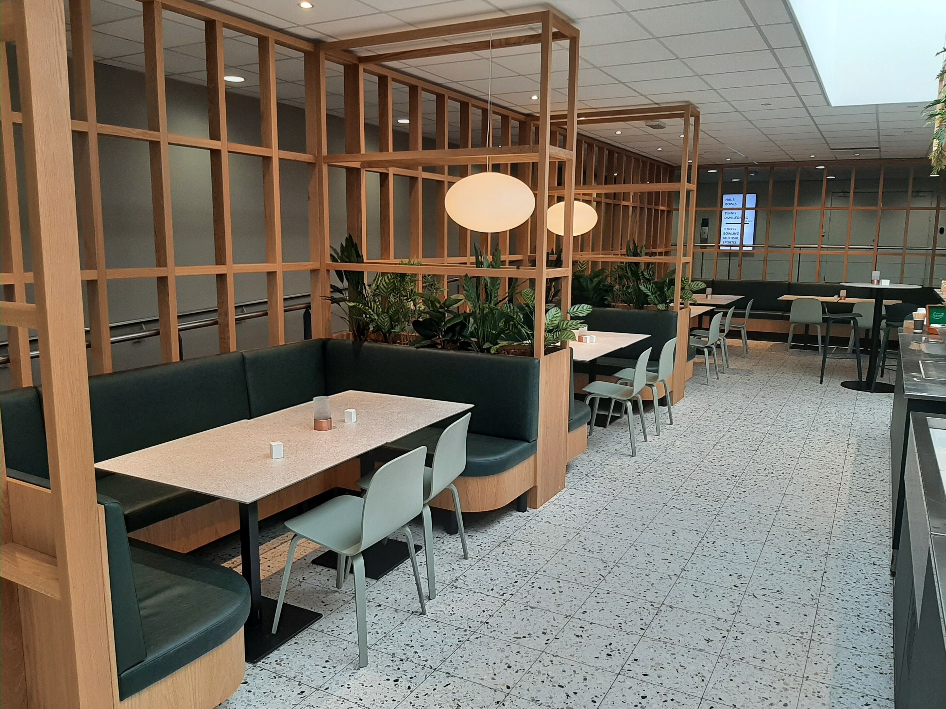 Un restaurante moderno con separadores de madera, asientos acolchados verdes y suelo de baldosas.