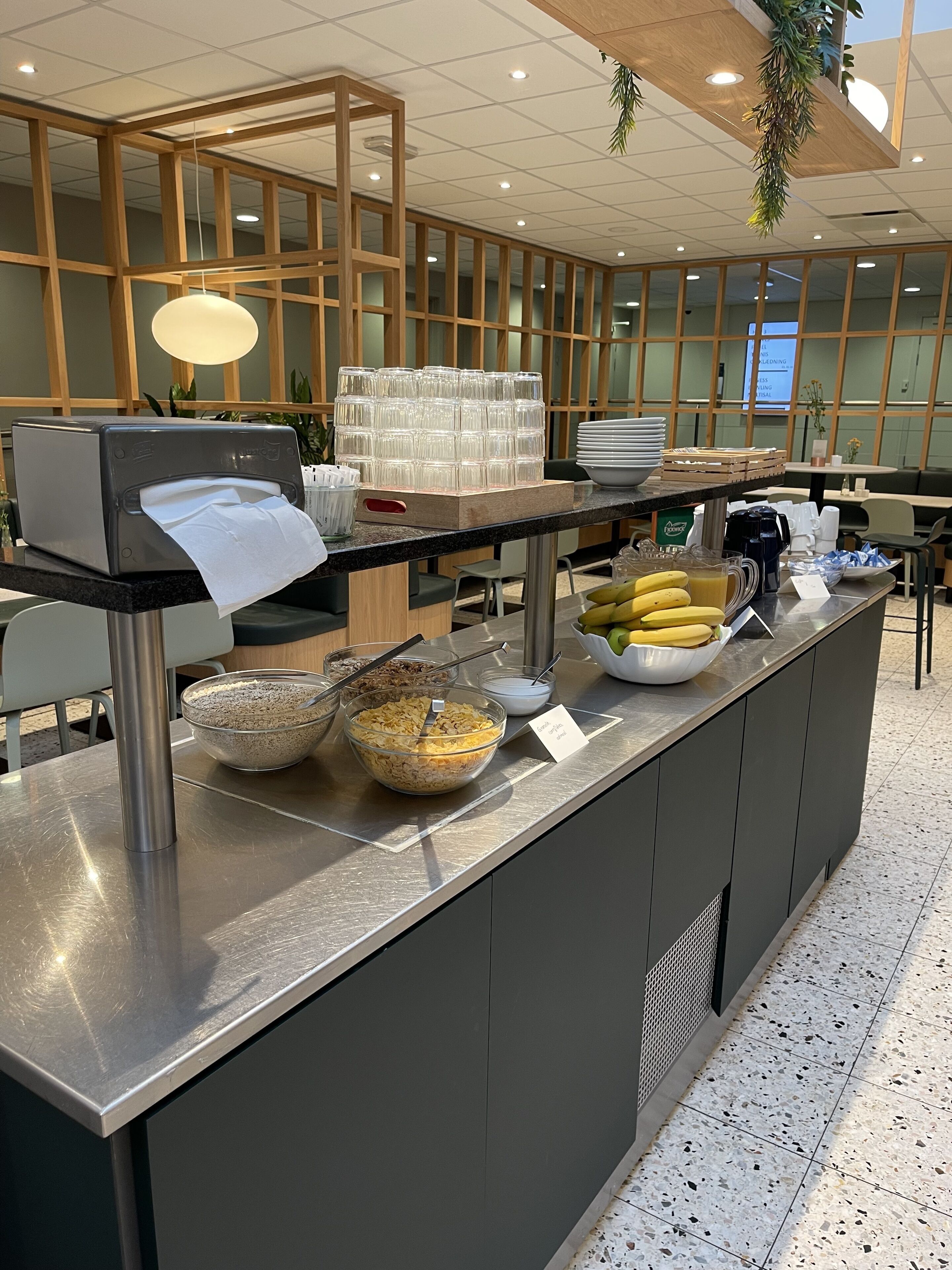 A buffet area with a variety of food items, including bowls of cereal and fruits, and a stack of plates.