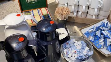 Estación de café y té con varias máquinas de café, vasos desechables y un recipiente con sobres de café.