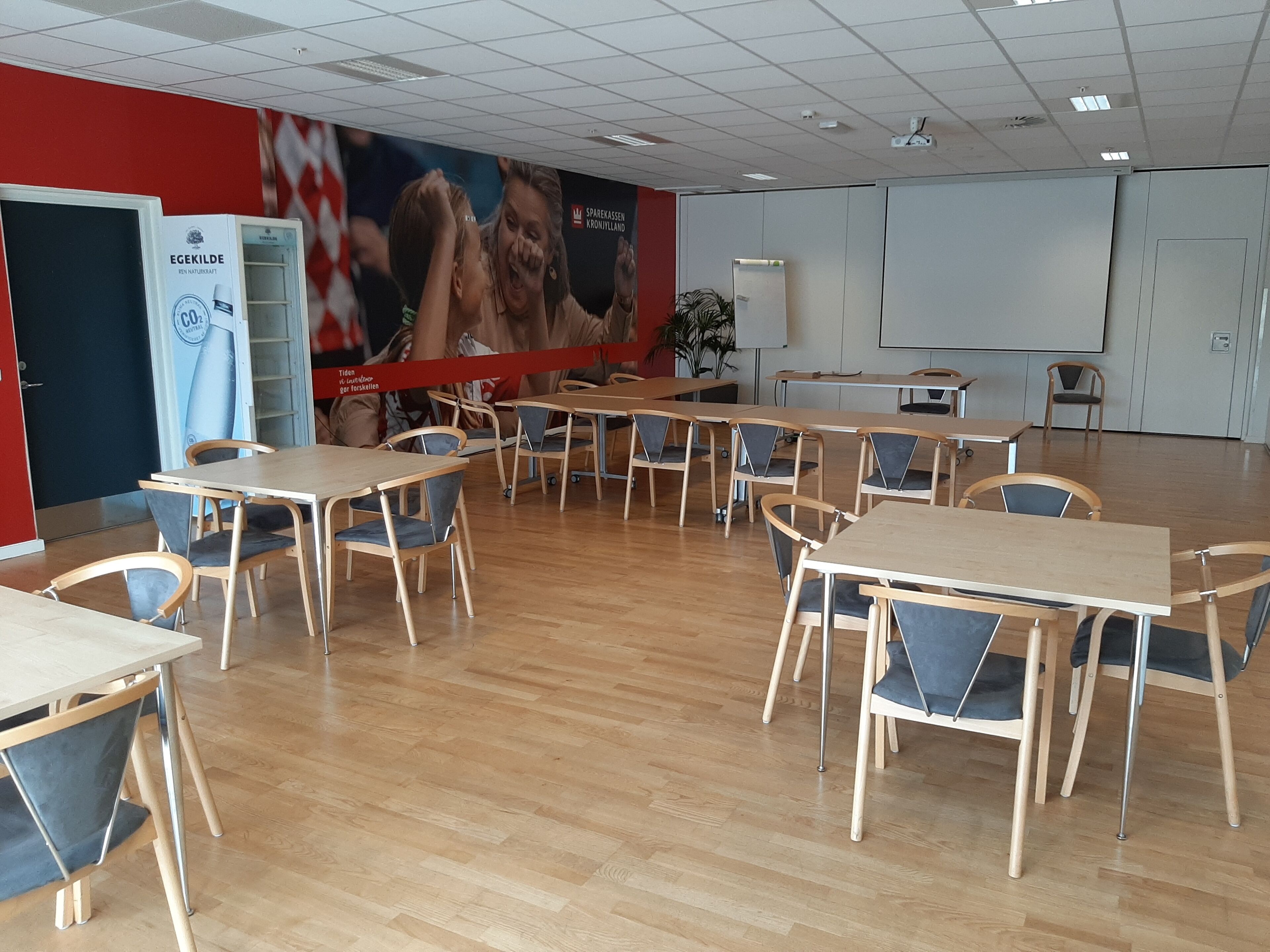 A conference room with wooden tables and chairs, a whiteboard, and a large poster on the wall.