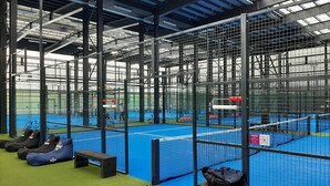 Instalación deportiva interior con varias áreas cerradas, césped artificial y bancos para sentarse.