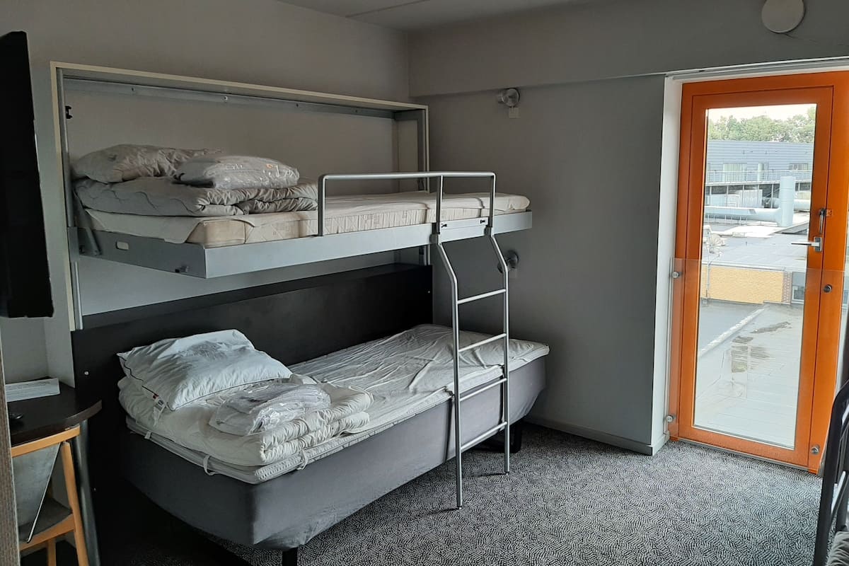 Une chambre avec des lits superposés, un bureau et une porte donnant sur un espace extérieur.