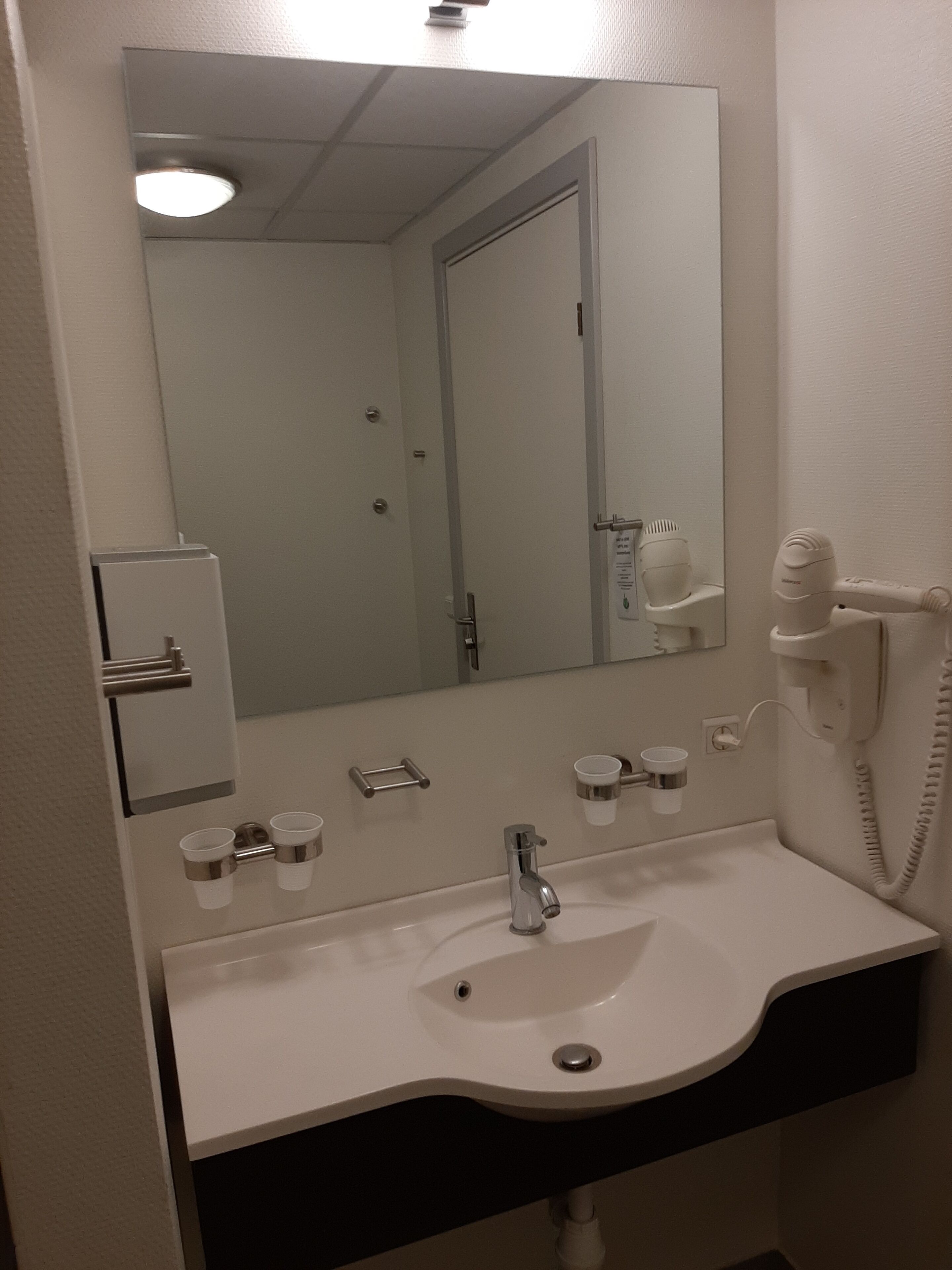 Un baño con lavamanos blanco, espejo, secador de pelo y teléfono.