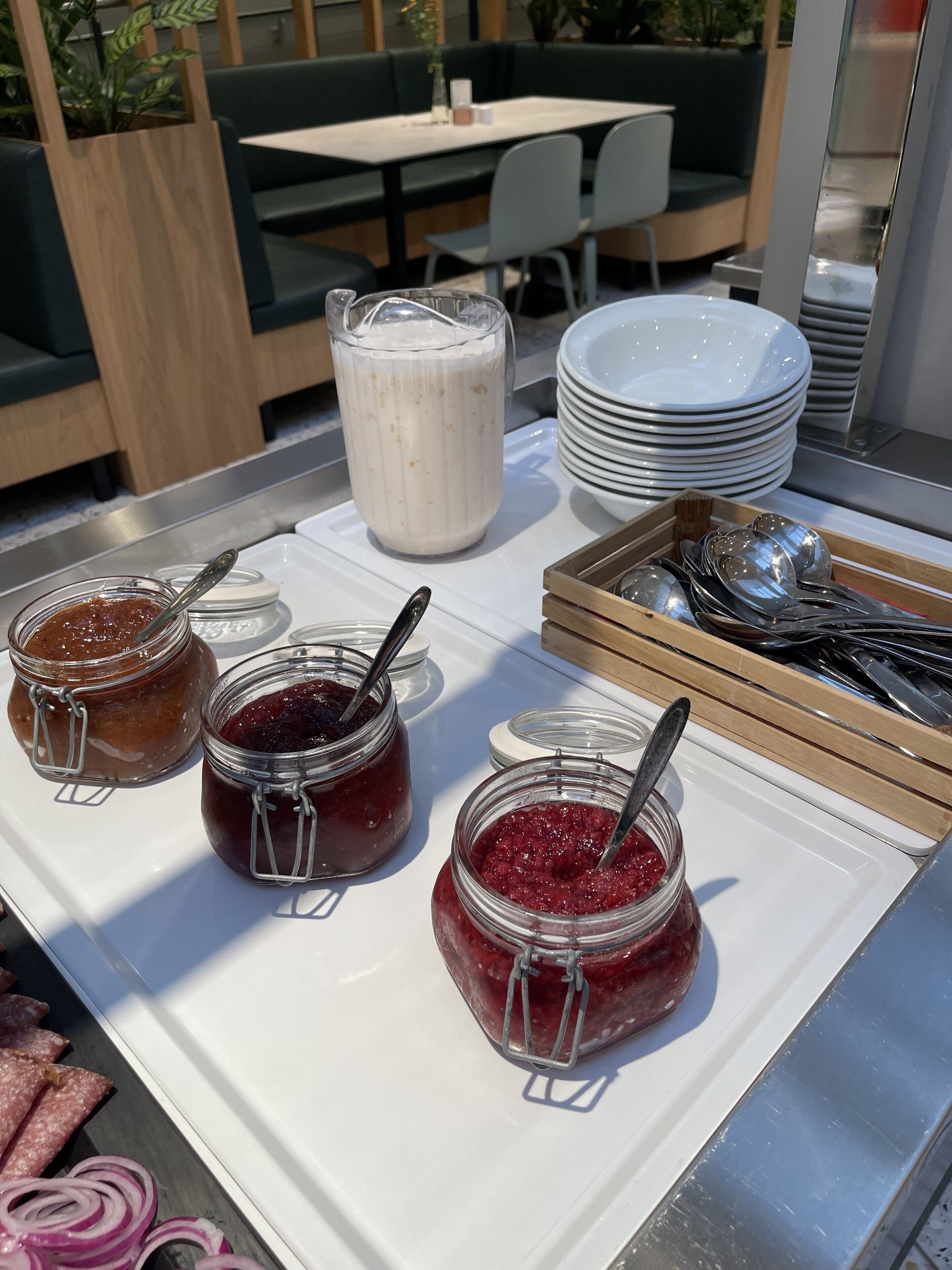 Un buffet de petit-déjeuner avec des pots de confiture, un pichet de lait et des assiettes empilées.