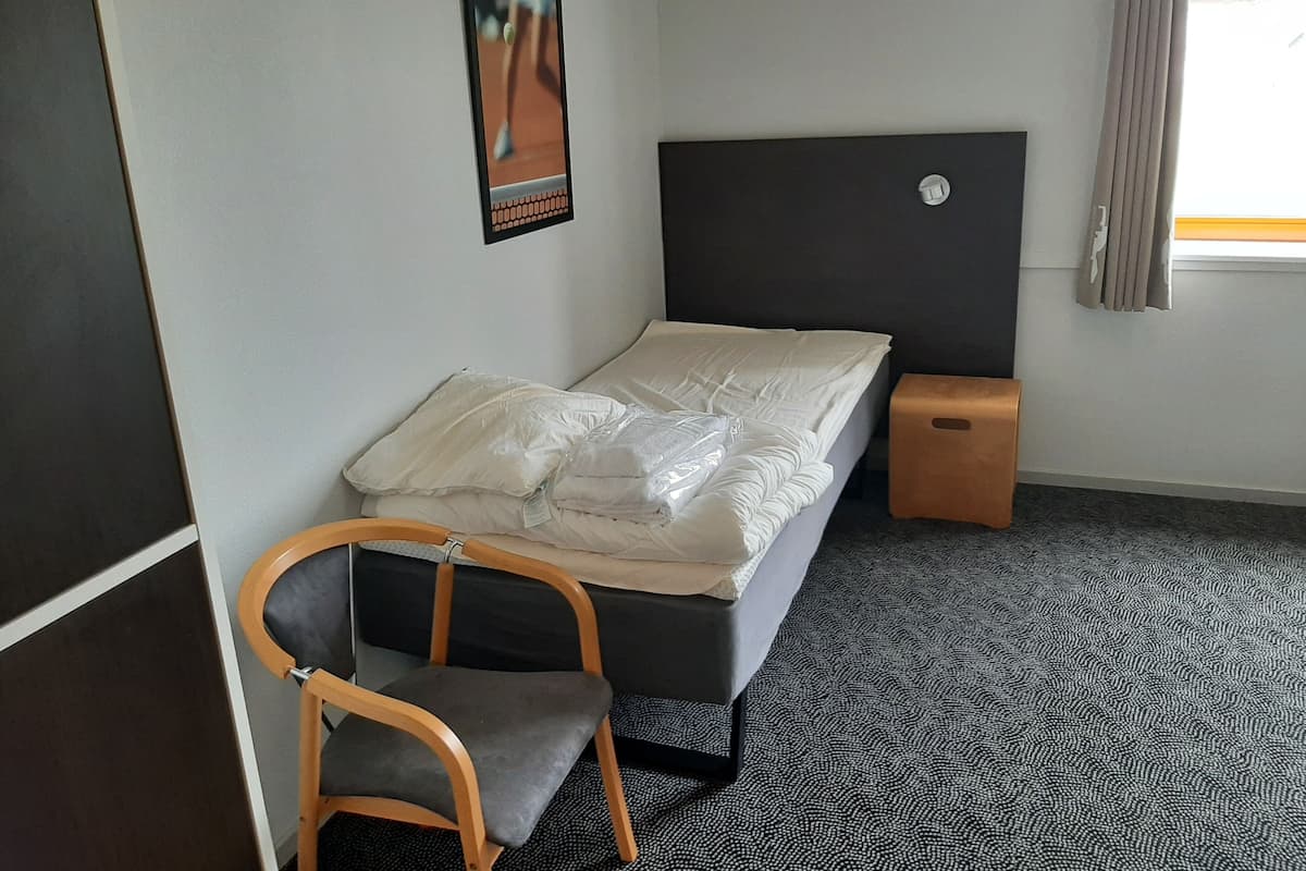 Une petite pièce, bien rangée, avec un lit simple, une chaise, une petite table et une affiche accrochée au mur.