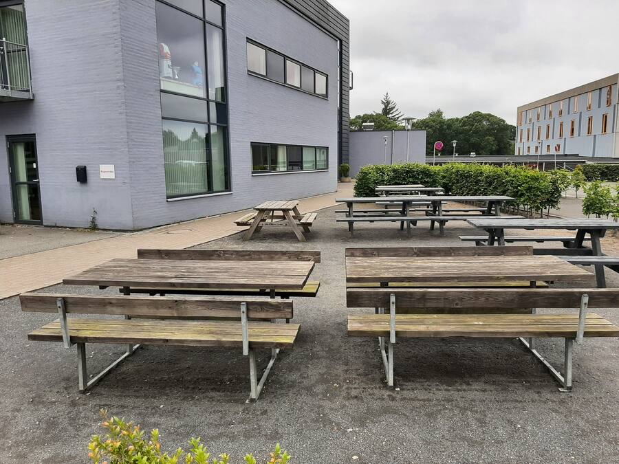 An outdoor seating area with picnic tables and benches, a building with large windows, and a sign indicating a no parking zone.