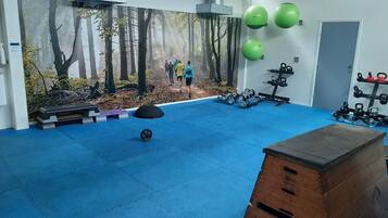 Une salle de sport avec des tapis bleus, du matériel d’exercice et une fresque représentant une forêt.