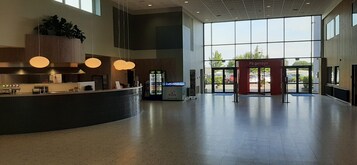 En rummelig lobby med en receptionsdisk, en automat og en stor glasdør, der fører udendørs.