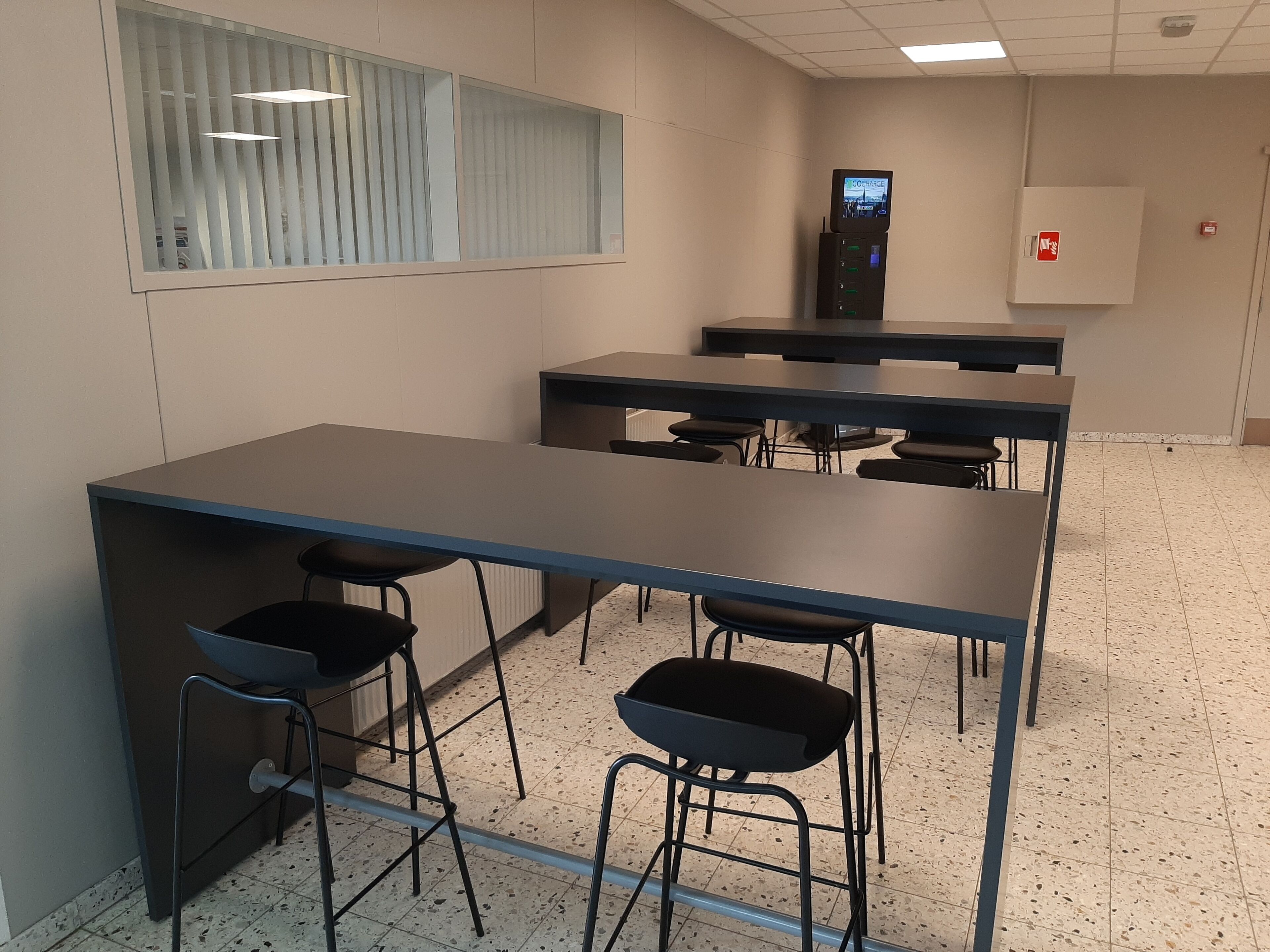 A conference room with a long table, four chairs, and a charging station.