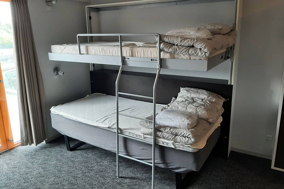 Une chambre avec un lit superposé, une fenêtre, des rideaux et un radiateur.