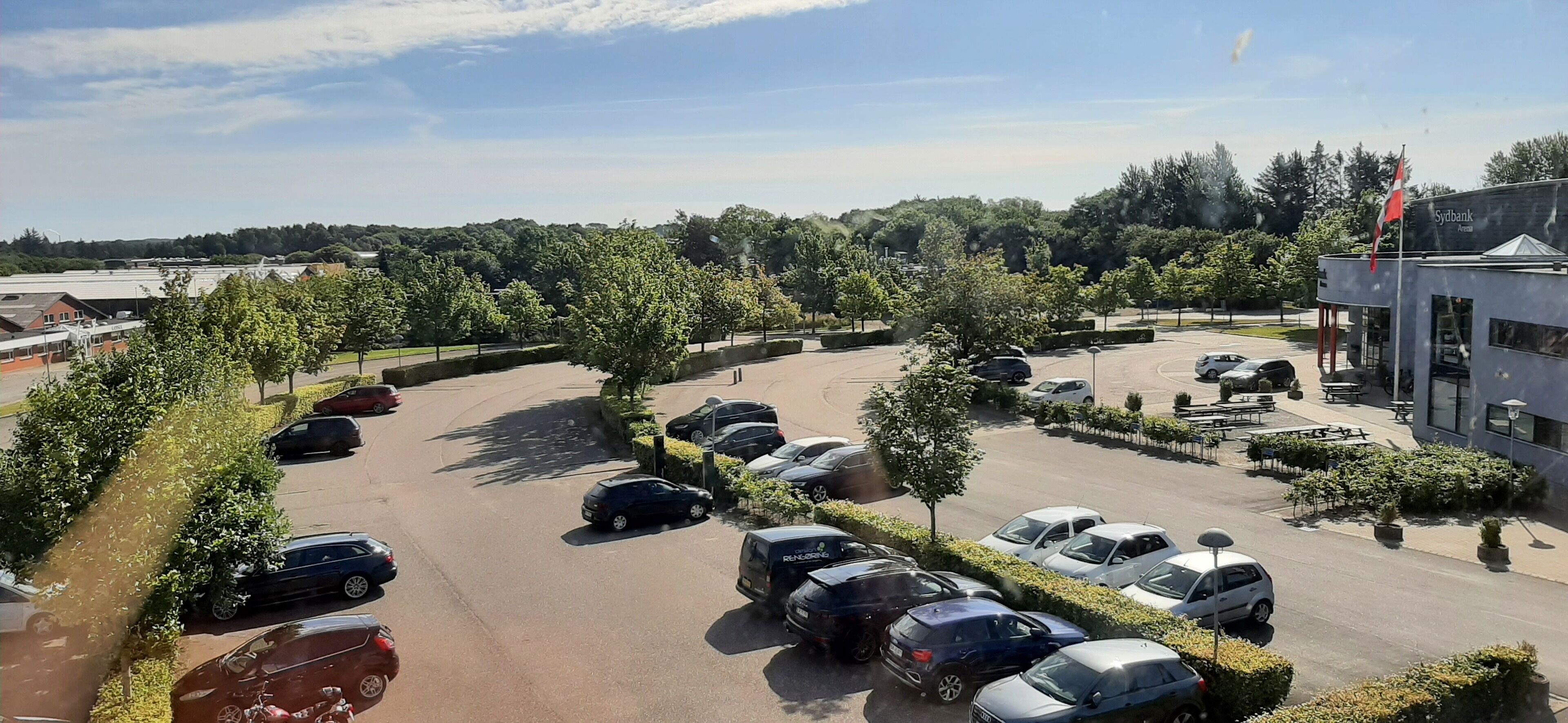 A parking lot with multiple cars, trees, and a building labeled 'Sydbank'.