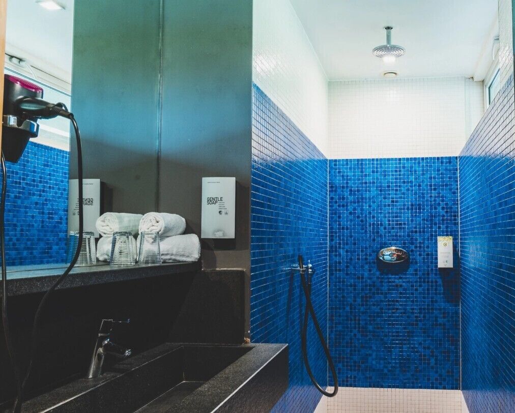 A bathroom with blue mosaic tiles, a shower, a sink with a mirror, and towels.