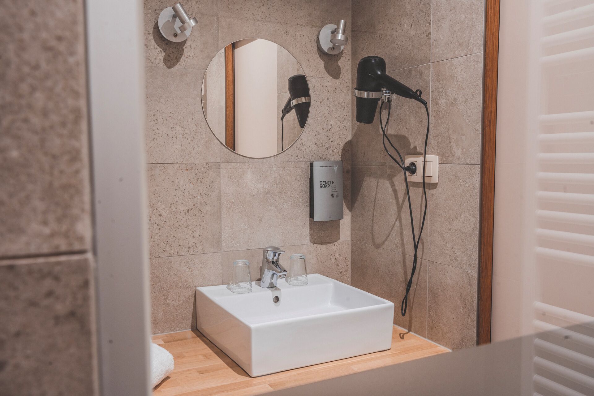 A bathroom with a white sink, two mirrors, a hairdryer, and a soap dispenser.