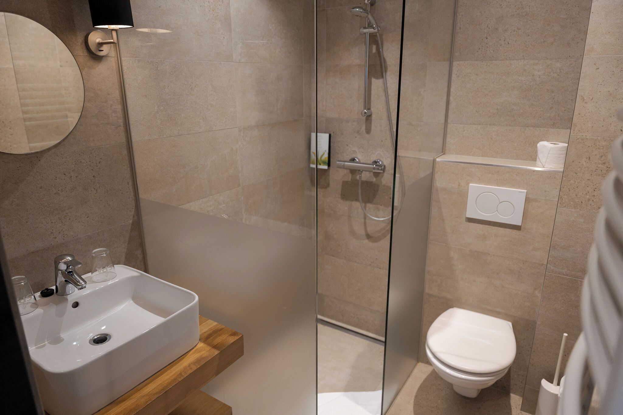 A modern bathroom with a glass-enclosed shower, a white sink with a wooden shelf, and a white toilet.