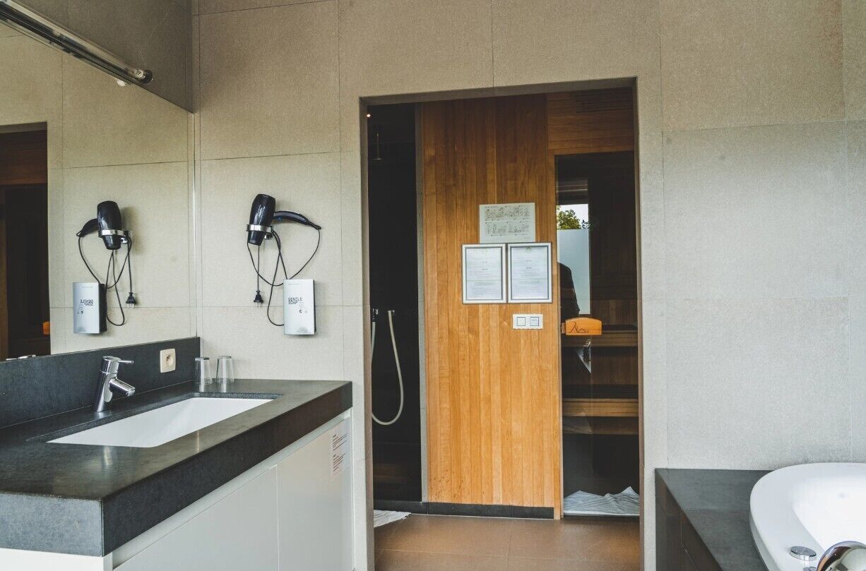 Un baño moderno con un lavamanos grande, dos secadores de pelo, una puerta de madera y una zona de ducha.