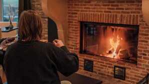 Iemand zit voor een open haard, met een bakstenen muur en een raam op de achtergrond.