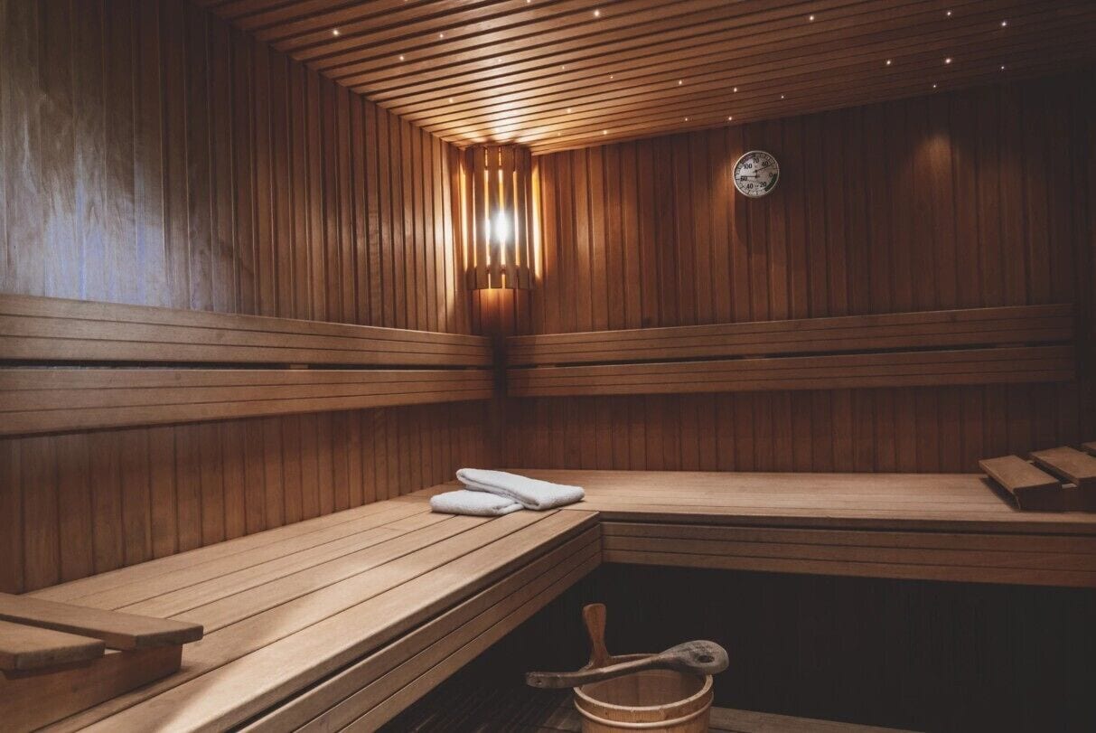 Eine Sauna mit Holzbänken, einer Wanduhr und einem Holzeimer.