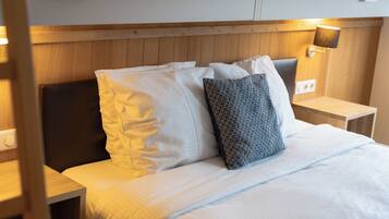Cama bem arrumada com almofadas brancas e estampadas, cabeceira de madeira, mesas de cabeceira com luminárias e painel de parede em madeira.