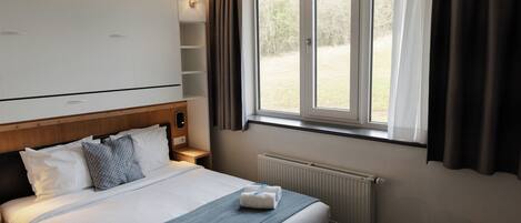 Una habitación de hotel con una cama, una ventana con cortinas, un radiador y un armario.