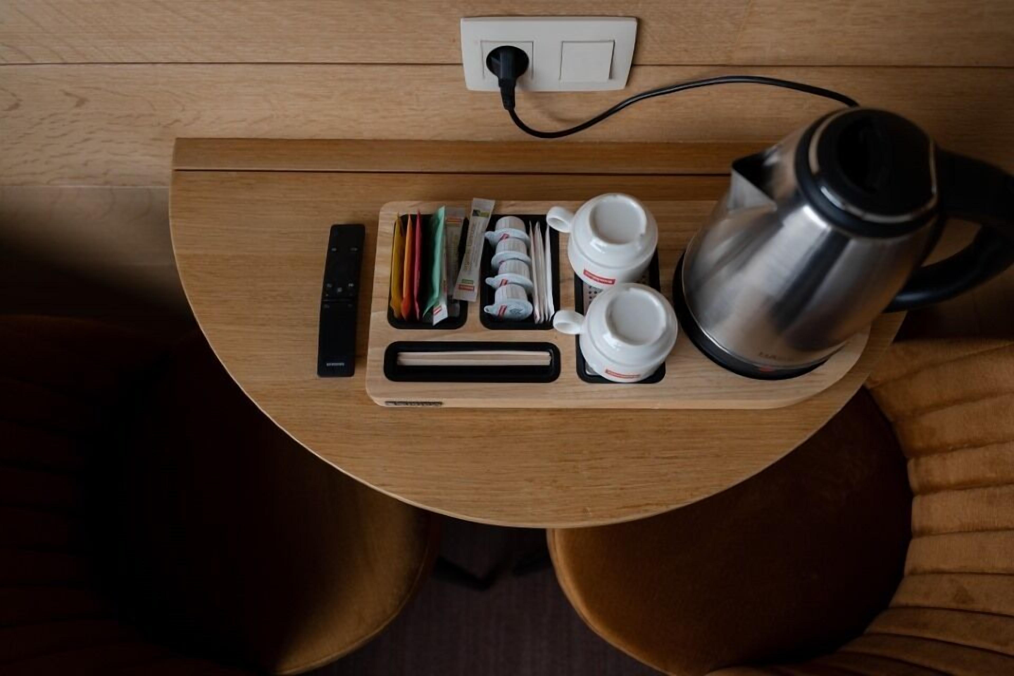 A wooden table with a power outlet, a kettle, cups, and a tray with pens and tissues.