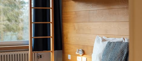 A bunk bed room with a wooden headboard, a bedside table with a lamp, and a window with a view of trees.