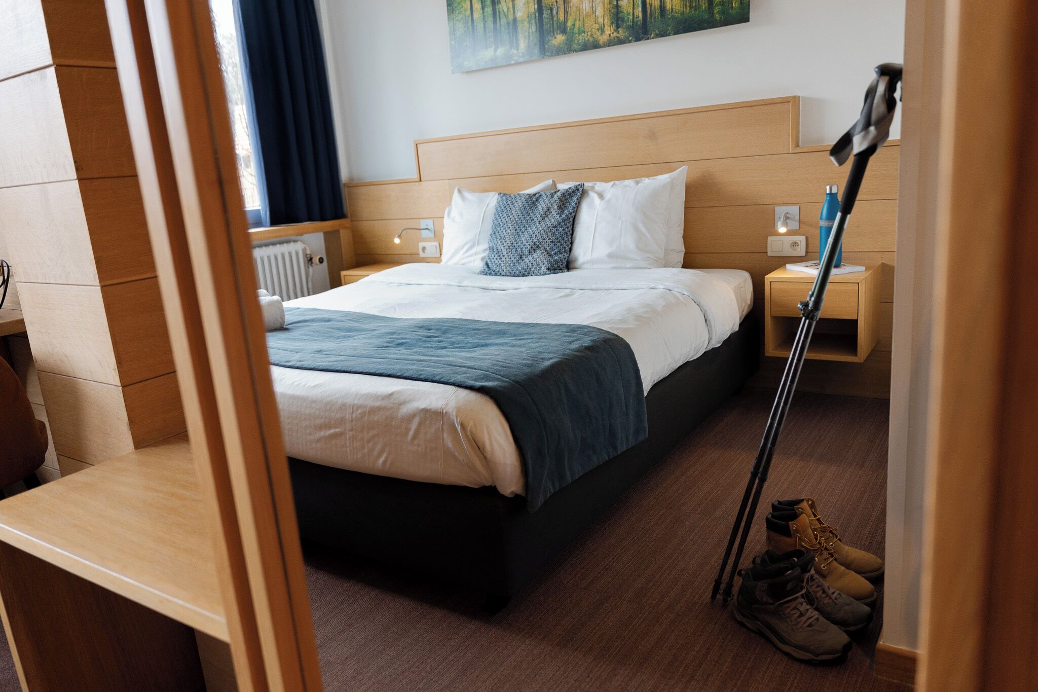 Une chambre d’hôtel avec un lit, des tables de chevet, une petite table, une lampe et une paire de bottes.