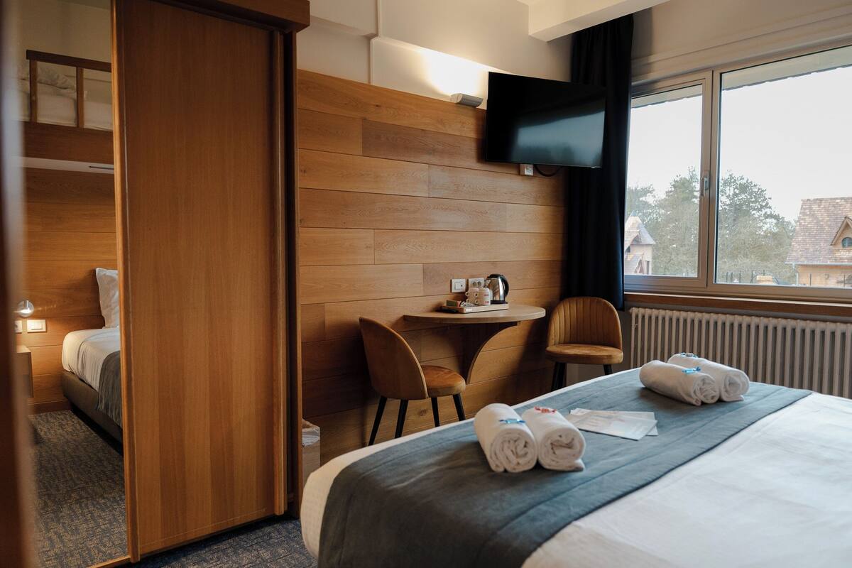 Une chambre d’hôtel équipée d’un lit, d’un bureau, d’une chaise, d’une télévision et d’une fenêtre donnant sur un paysage agréable.