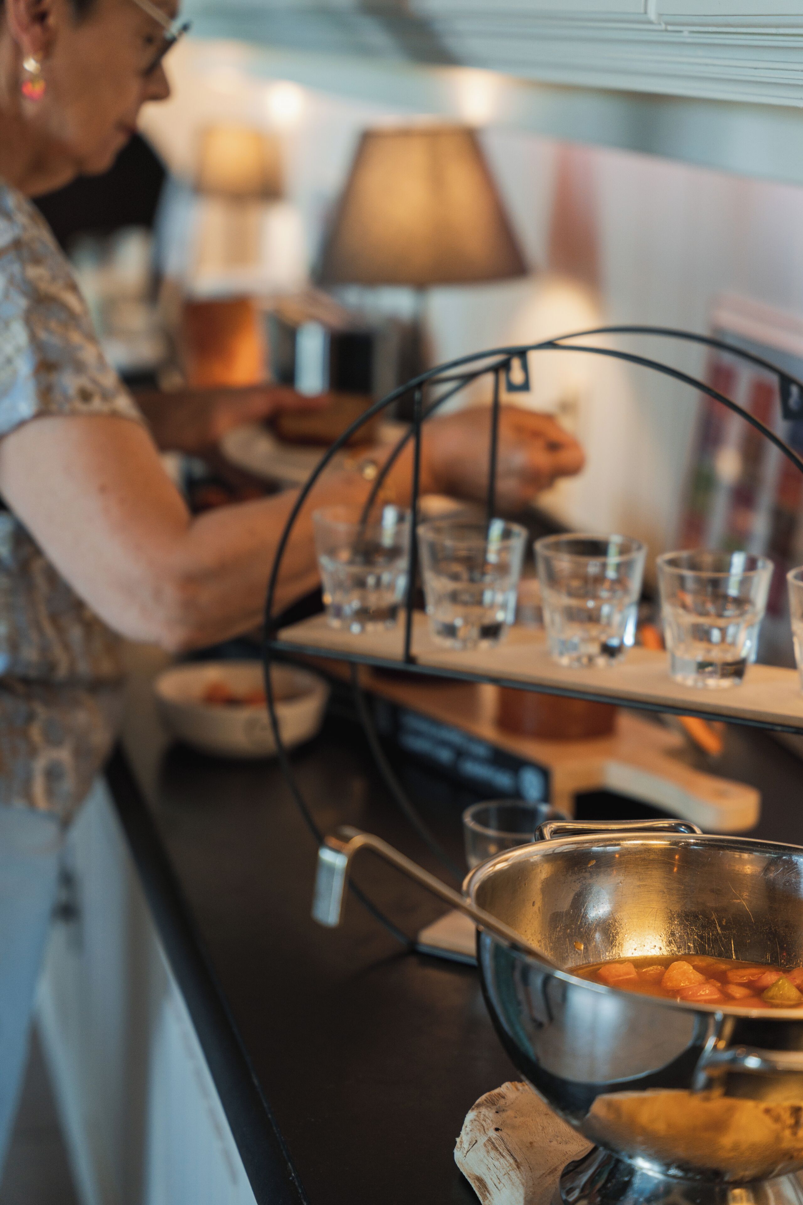A kitchen counter with a metal bowl, glasses, and a person preparing food.